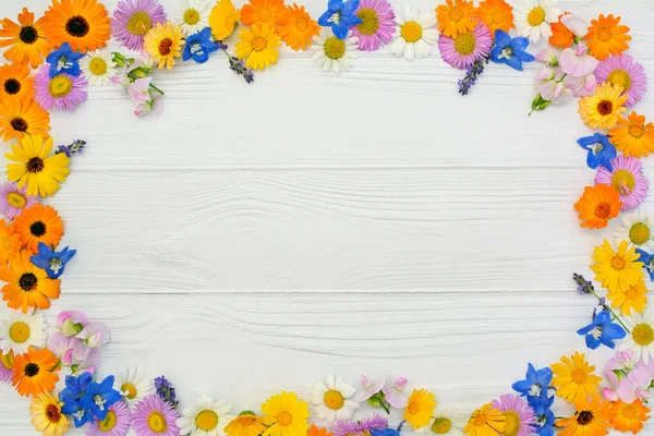 Açık ahşap zemin üzerinde sarı, mavi, pembe ve beyaz çiçeklerden yapılmış bir çerçeve. Paskalya, bahar, yaz konsepti. Üst görünüm, alanı kopyala