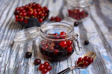 Reçelli cam kavanoz ve kırsal ahşap arka planda kırmızı frenk üzümü dalları. Mevsimlik meyveler. Kapat.