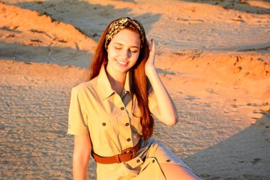 Güzel bir genç kız kumların arkasında oturur ve hayal kurarak gülümser. Portre