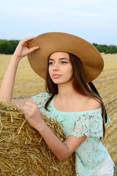 Retrato de uma jovem em um chapéu de palha contra um fundo de palheiro. — Fotografia de Stock