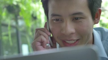 4k: Genç Asyalı işadamı cep telefonunuzda konuşurken bir dizüstü bilgisayar kullanarak