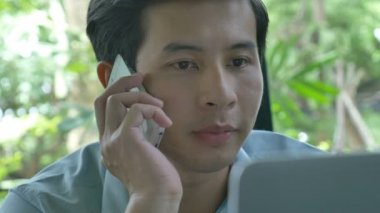 4k: Genç Asyalı işadamı cep telefonu konuşurken bir dizüstü bilgisayar kullanarak