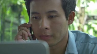 4k: Genç Asyalı işadamı cep telefonu konuşurken bir dizüstü bilgisayar kullanarak