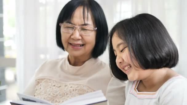快乐的亚洲祖母和可爱的女孩在家里看书 Fps — 图库视频影像