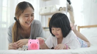 Yavaş hareket 4k Lovely küçük Asyalı kız ve annesi kumbara kaydetmek için para koyarak