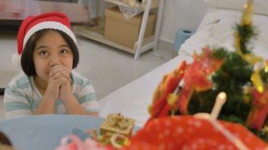4 k Asyalı çocuk Noel için dua Noel ağacı sunar. Noel Baba şapkası, küçük bir kız dua ediyor
