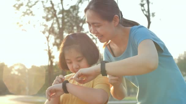 幸せなアジア娘と母の健康を設定は 公園で一緒に実行する前にリストバンドをスマート スローモーション撮影 — ストック動画