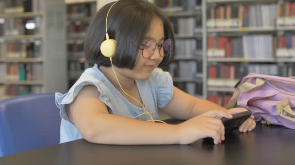Asian Student Słuchania Muzyki Przez Słuchawki Szkolnej Bibliotece Dolly Strzał — Wideo stockowe