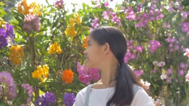 Güneşli bir gün yaz bahçesinde çiçeklenme çiçekler zevk mutlu Asyalı kız, yavaş hareket çekim