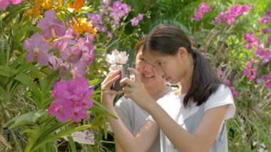 Mutlu Asyalı kız ve anne çiçeklenme çiçekler zevk ve birlikte bir fotoğraf çekmek, yavaş hareket çekim