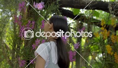 Güneşli bir gün yaz bahçesinde çiçeklenme çiçekler zevk mutlu Asyalı kız, yavaş hareket çekim