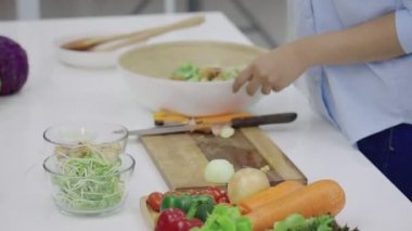 Mutfaktaki bir kasede sebze salatası karıştıran kadın ellerinin yakın çekimi.