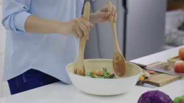 Mutfaktaki bir kasede sebze salatası karıştıran kadın ellerinin yakın çekimi.