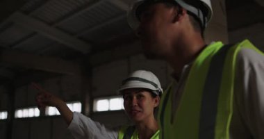 Sert Şapkalı Asyalı Endüstriyel Mühendisler. İnşaat alanında birlikte çalışan güvenlik ceketi giyiyorlar.