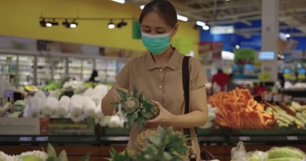 スローモーションアジアの女性が果物や野菜部門でスーパーマーケットの棚から果物を選ぶ医療用マスクを着用 — ストック動画