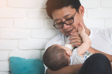 Güzel bir an. Onun bebek tutan ve onu beslerken gülümseyen hoş Genç Asyalı babası.