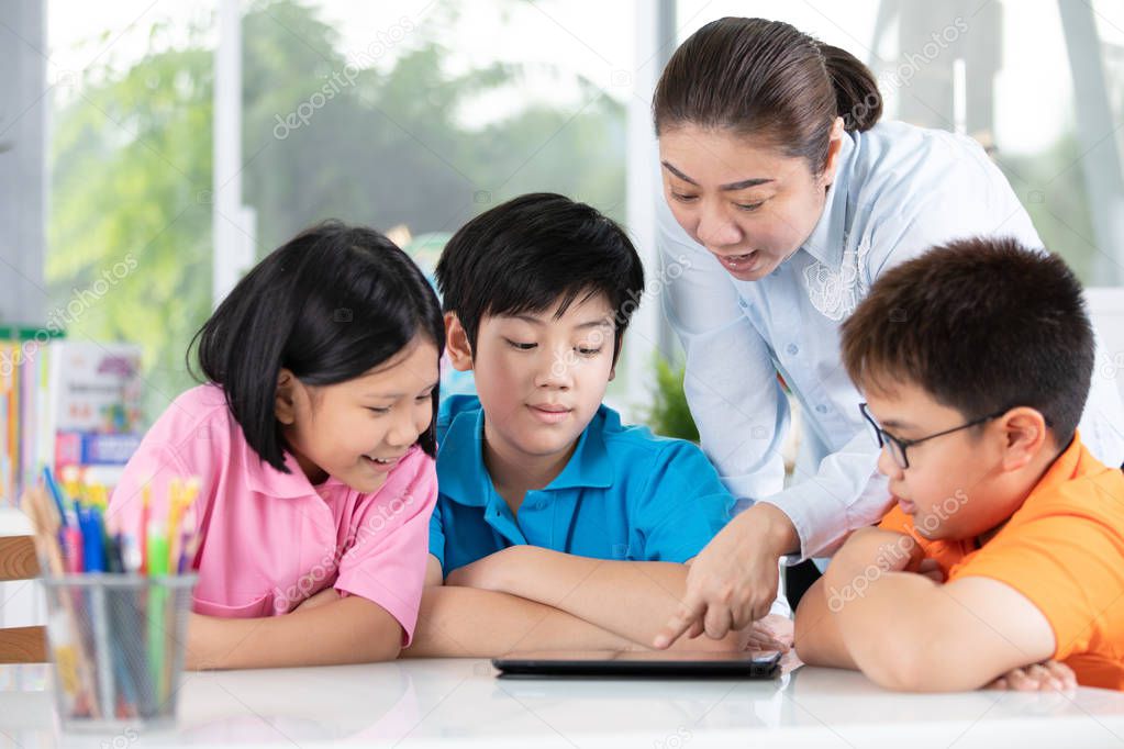 Close uo of asian teacher and Three kids entertaining themselves using digital tablet