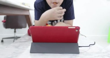Uzun sandalye ve çizgi film tablet bakar çocuk gevşeme içine dolly ve patates cipsi evde yemek.