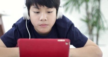 Asyalı çocuk tablet bilgisayar ve kulaklık ev ödevlerini yapıyor.