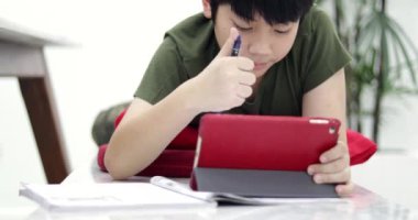 Asyalı çocuk tablet bilgisayar ve kulaklık ev ödevlerini yapıyor. Dolly taşıma sağdan sola.