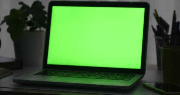 Ordinateur portable avec écran vert. Bureau sombre. Dolly à l'intérieur. Parfait pour mettre votre propre image ou vidéo .