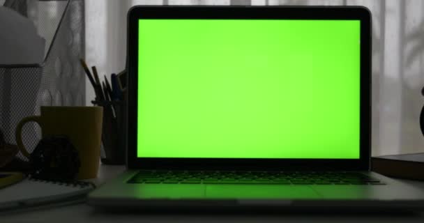Ordinateur portable avec écran vert. Bureau sombre. Dolly de gauche à droite. Parfait pour mettre votre propre image ou vidéo .