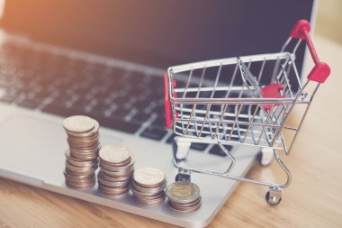 Sikke laptop ve çalışma alanı kullanarak evdekilerle online alışveriş veya teknoloji arka plan kavramları pazarlama olarak, ahşap masa üzerinde küçük alışveriş sepeti içerir.