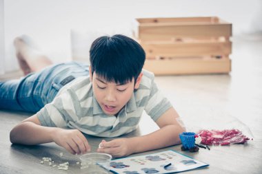 Happy asian boy lying and playing plastic block at home clipart