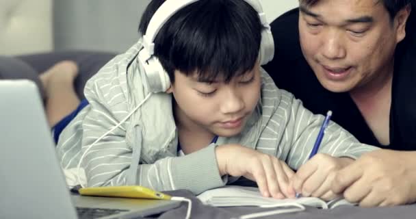 アジアの父の前面からドリー撮影彼の若い息子を助けるは 少年は自宅に彼の宿題をしている間 — ストック動画