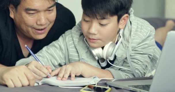 少年は自宅に彼の宿題をやっている間 アジアの父は彼の若い息子を手伝ってください — ストック動画