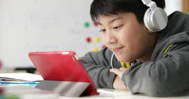アジアの若い男の子でドリーを自宅でヘッドホンでタブレット コンピューターで遊んで — ストック動画