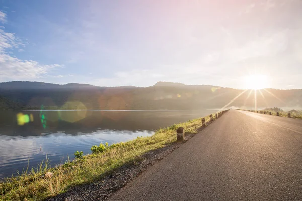 Asfalt yol ile rezervuar açıkça mavi gökyüzü ve dağlar Huaiprue depo, Nakhon Nayok Tayland arka planda parlama ile.