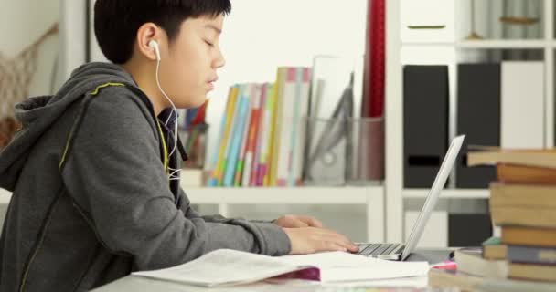 かわいいアジアの十代の男の子のラップトップ コンピューターを自宅で宿題をやっています — ストック動画