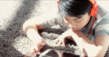 Mutlu Asyalı çocuk yalan üzerinde halı oynarken oyun üzerinde dijital Tablet evde