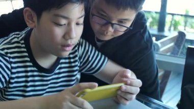 Yavaş hareket 4 k mutlu Asyalı çocuk birlikte akıllı telefonda mobil oyunu online oynamak. Çocuk ve arkadaş eğlenmek stratejisi ile görüşmek.