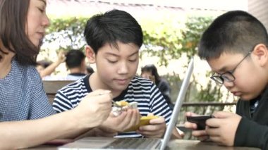 Yavaş hareket 4k Asya anne oğluna pasta beslemek. İki çocuk smartphone telefon oyun oynuyor 