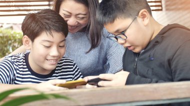 Mutlu Asya Aile Anne ve oğlu cep telefonu gülümsemek yüz ile birlikte izlerken.