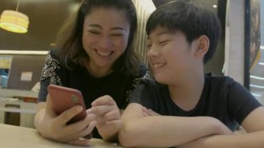 4 k Slow motion mutlu Asyalı çocuk ve annesi ile akıllı telefon, izlerken yüzünü gülümseme .