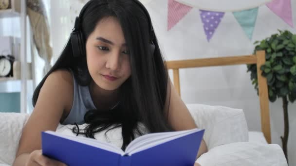 スローモーション 本ベッド ルーム 読書でベッドで休んで 笑顔でカメラを見て美しいアジア女の子の — ストック動画