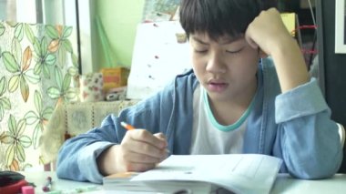 Ağır çekim Sevimli Asya çocuğun ödevlerini kızgın yüzü ile yapıyor. 4k