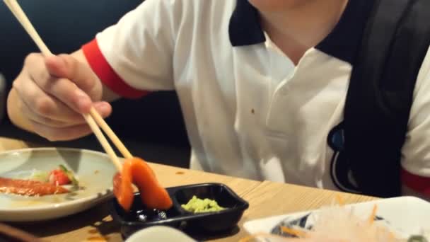 快乐的亚洲男孩吃日本料理的慢动作 一个十几岁的孩子坐在咖啡馆里吃寿司 — 图库视频影像