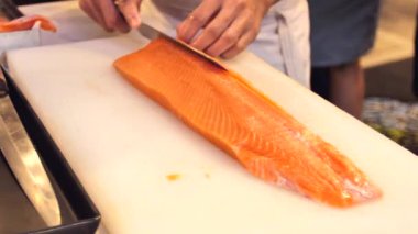 Suşi şefi Close-up yetenek dilim taze somon bir suşi barda göster. Profesyonel aşçı kesim balık fileto ticari mutfak, ağır çekim.