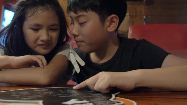 快乐的亚洲孩子在咖啡馆或餐厅选择饮料和食物的菜单 兄妹在餐馆的慢动作 — 图库视频影像