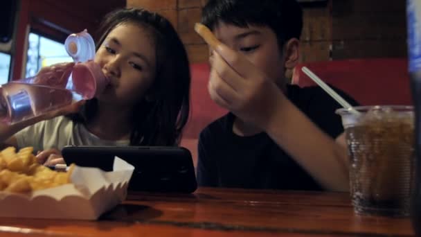 携帯電話で見て幸せなアジアの子ジャガイモ火災 兄と妹のレストランでのスローモーションを食べてお楽しみください — ストック動画