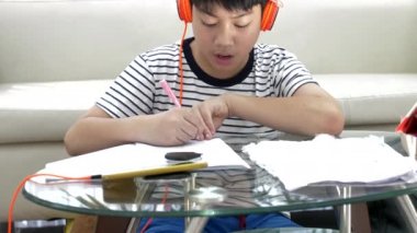 Asyalı çocuk gereçleri kulaklık ve oturma odasındaki masada ödev .