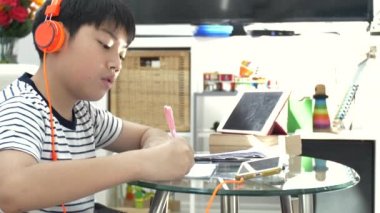 Asyalı çocuk gereçleri kulaklık ve oturma odasındaki masada ödev .