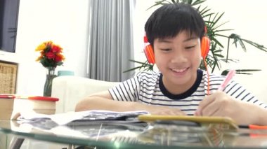 Asyalı çocuk gereçleri kulaklık ve oturma odasındaki masada ödev .