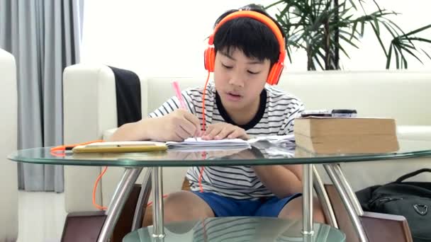 Азиатский Мальчик Наушниках Выполняет Домашнюю Работу Столе Гостиной — стоковое видео