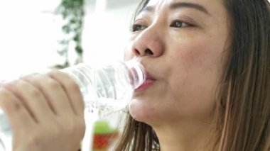 Asyalı kadın şişe maden suyu içiyor. Uzun saç içecekler ile güzel kız temiz su. Yavaş hareket 4k