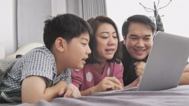 Mutlu aile baba anne ve dizüstü bilgisayarda izlemek ve having fun, yavaş hareket 4 k Asya Aile dinlenme yatakta dizüstü bilgisayar ile oğlu